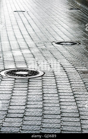 Fognatura di acciaio chiusino sul bagnato scuro cobblestone pavement Foto Stock