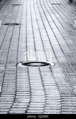 Fognatura di metallo chiusino sul bagnato scuro cobblestone pavement Foto Stock