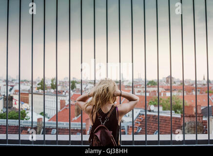 Giovane donna guardando attraverso le ringhiere, a vista sui tetti, vista posteriore Foto Stock