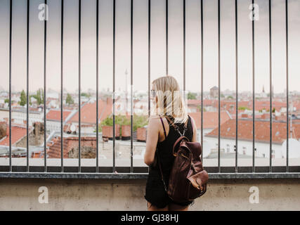 Giovane donna guardando attraverso le ringhiere, a vista sui tetti, vista posteriore Foto Stock