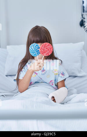 Ritratto di ragazza paziente tenendo lecca-lecca davanti agli occhi in ospedale per bambini ward Foto Stock
