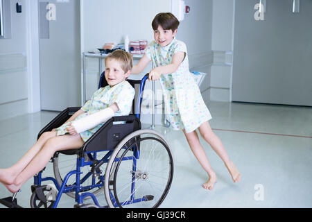 Ragazzo pazienti spingendo amico in carrozzella in ospedale per bambini ward Foto Stock