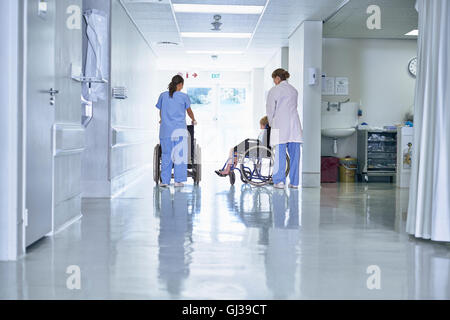 Vista posteriore del medico spingendo ordinata bambino paziente in carrozzella in ospedale per bambini ward Foto Stock