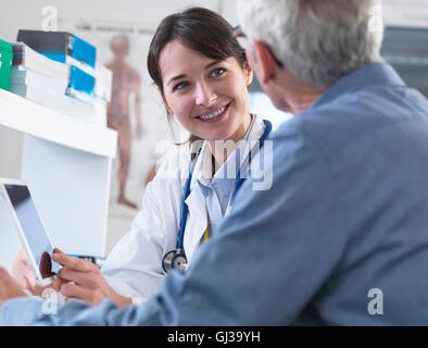 Medico sanitaria la condivisione di informazioni sulla tavoletta digitale con paziente in clinica Foto Stock