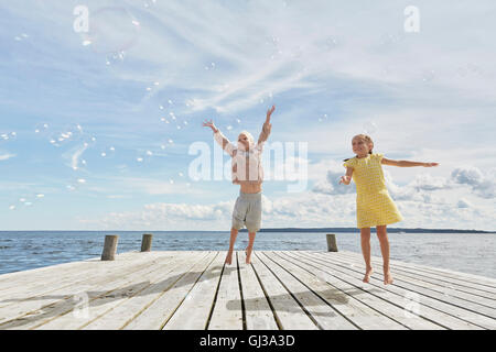 Due giovani amici sul molo in legno, saltando per raggiungere le bolle Foto Stock