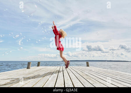 Giovane ragazza sul molo in legno, saltando per raggiungere le bolle Foto Stock