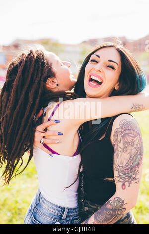Tatuato giovani donne ridere e abbracciando in parco urbano Foto Stock