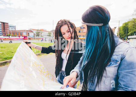 Due giovani donne con dreadlocks e capelli tinti puntando alla mappa in parco urbano Foto Stock