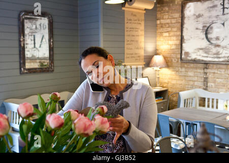 Femmina matura cliente menu di lettura mentre parli sullo smartphone in cafe Foto Stock