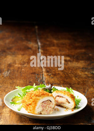 Kiev di pollo con formaggio e prosciutto riempimento sulla piastra bianca verde con foglie di insalata, vintage tavolo in legno Foto Stock