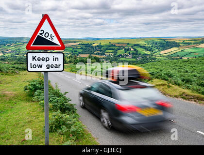 Un Holiday Maker's car scende giù per una ripida collina nella campagna, passando un cartello di avviso visualizzando il gradiente . Foto Stock