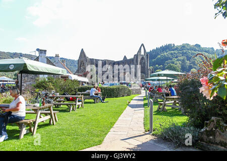 La gente seduta al di fuori su tavoli da picnic in background sono le rovine di Tintern Abbey Monmouthshire Wales UK Foto Stock