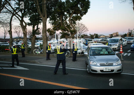 Come il sole scende, squadre di resa uniforme per il controllo del traffico aereo steward, con luminosi wands, aiuti agli automobilisti di ottenere dal Nakayama R Foto Stock