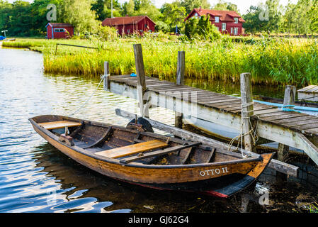 Pataholm, Svezia - Agosto 9, 2016: Tradizionale skiff di legno chiamato Ottone II ormeggiata al piccolo molo con red homestead in backgro Foto Stock