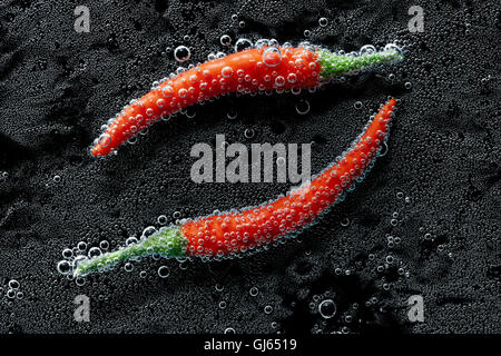 Peperoncino in un acqua minerale, una serie di foto. Close-up di acqua gassata su sfondo nero Foto Stock