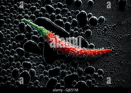 Peperoncino in un acqua minerale, una serie di foto. Close-up di acqua gassata su sfondo nero Foto Stock