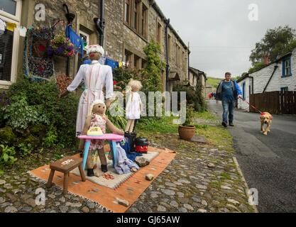 Un uomo cammina davanti ad una famiglia di scarecrows durante il Kettlewell Spaventapasseri Festival in North Yorkshire. Foto Stock