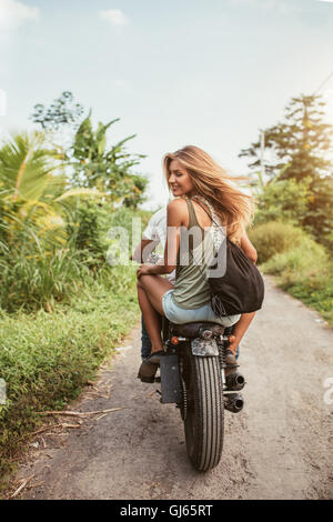 Vista posteriore del colpo di coppia giovane in sella moto su strada sterrata. Bella giovane donna seduta sul retro del suo ragazzo in sella moto Foto Stock