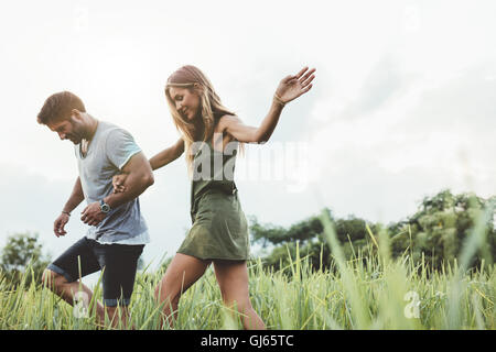 Colpo all'aperto di coppia giovane passeggiate attraverso prati mano nella mano. Uomo e donna che parlano a piedi attraverso il campo di erba in campagna. Foto Stock