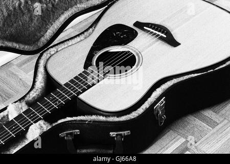 Vecchia chitarra appoggiata nella sua morbida custodia rigida. ISO800. Immagine filtrata per sgranate in bianco e nero. Foto Stock