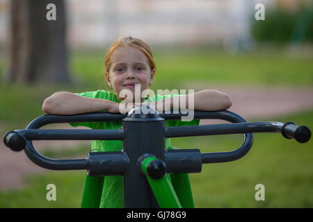 Ritratto di bambina seduta su attrezzatura ginnica nel parco pubblico. Foto Stock