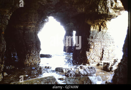 Sunny View del mare di acqua di lavaggio attraverso piccoli archi all'interno del calcare magnesiaco basamenti di Marsden Rock, Marsden Bay, South Shields, Inghilterra del Nord Est, nell'estate del 1975 Foto Stock