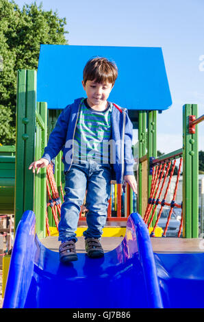 Un giovane ragazzo gioca su una diapositiva in un parco giochi per bambini. Foto Stock