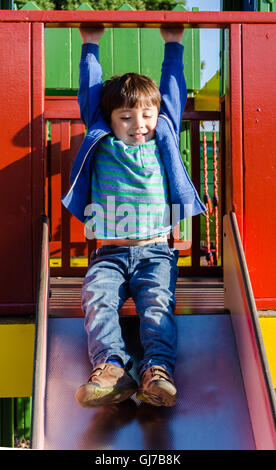 Un giovane ragazzo gioca su una diapositiva in un parco giochi per bambini. Foto Stock