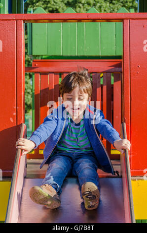 Un giovane ragazzo gioca su una diapositiva in un parco giochi per bambini. Foto Stock