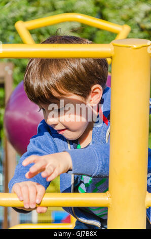 Un giovane ragazzo si arrampica su di un telaio di arrampicata in un parco giochi per bambini. Foto Stock