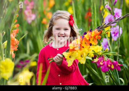 Little Girl holding gladiolus mazzo di fiori. Bambino picking fiori freschi in giardino. Bambini giardinaggio in autunno Foto Stock