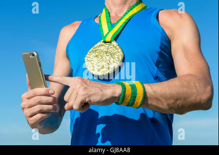 Brasiliano della medaglia d oro atleta con il giallo e il verde del Brasile di braccialetti di colore utilizzando il telefono cellulare contro il cielo blu Foto Stock