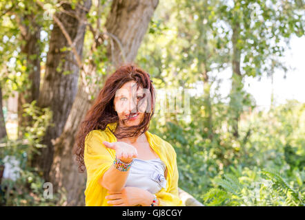 Struttura elegante e affascinante donna matura con scialle giallo e silver top è sorridente in un parco verde mentre mostra palm Foto Stock
