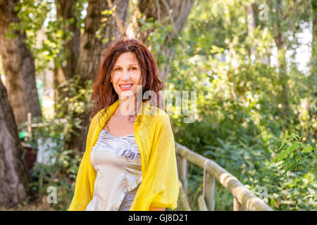 Struttura elegante e affascinante donna matura con scialle giallo e silver top è sorridente in un parco verde Foto Stock