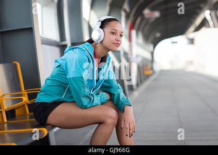 Modello rilasciato. Giovane donna seduta sulla piattaforma ferroviaria di indossare le cuffie. Foto Stock