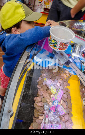 Un giovane ragazzo suona su un 2p slot machine in una galleria in un luogo di villeggiatura. Foto Stock