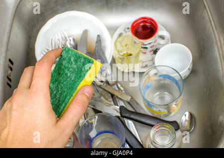 Faccende, lavaggio piatti nel lavandino con una spugna in mano Foto Stock