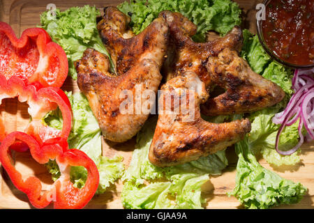 Ali di pollo con salsa di pomodoro e verdure su un tavolo di legno. Foto Stock