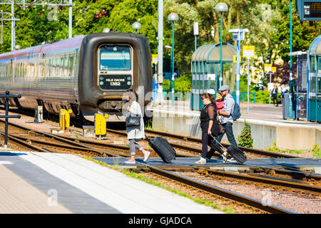 Kalmar, Svezia - Agosto 10, 2016: Persone con borse trolley attraversando le vie per raggiungere la piattaforma presso la stazione ferroviaria. Foto Stock