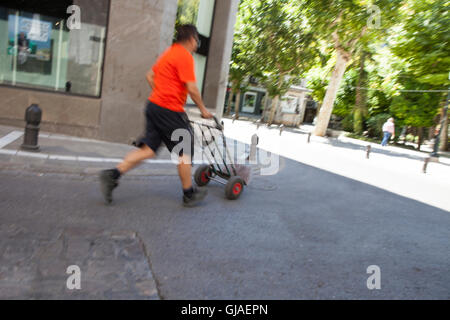 Coppia esegue la consegna uomo che porta un carrello su city centre street. Slow motion shot Foto Stock