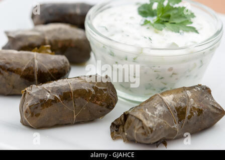 Dolma(tolma, sarma) in foglie di uva con carne serviti con salsa di yogurt e verdi su una piastra bianca closeup. Foto Stock