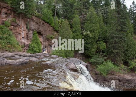 Un giovane uomo seduto in cima a una cascata di uva spina cade parco dello stato del Minnesota, Stati Uniti d'America. Foto Stock