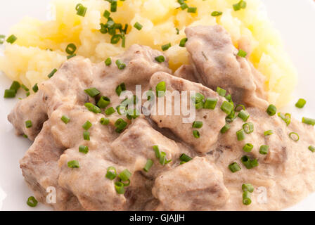 Carni bovine Stroganoff con purè di patate decorate con la cipolla verde sulla piastra bianca closeup. Foto Stock