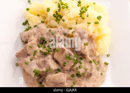 Carni bovine Stroganoff con purè di patate decorate con la cipolla verde sulla piastra bianca closeup. Foto Stock