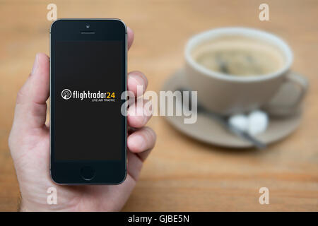 Un uomo guarda al suo iPhone che visualizza il Flightradar 24 logo, mentre sat con una tazza di caffè (solo uso editoriale). Foto Stock