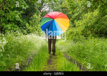 Persona che cammina nel bosco con grande ombrello colorato Foto Stock
