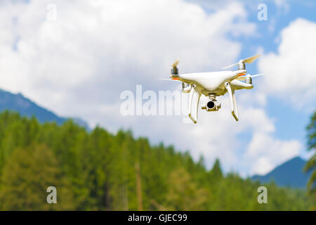 White drone quad copter con alta risoluzione Telecamera digitale volare nel cielo blu sopra la montagna Foto Stock