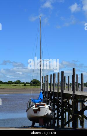 Singolo Yacht a vela arrotolata sulla terraferma da un pontile in legno sul fiume Wyre a Skippool Creek, LANCASHIRE REGNO UNITO Foto Stock