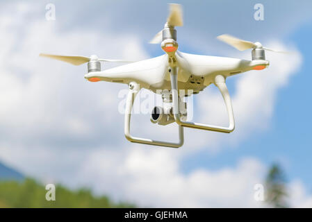 White drone quad copter con alta risoluzione Telecamera digitale volare nel cielo blu sopra la montagna Foto Stock