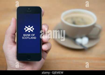 Un uomo guarda al suo iPhone che visualizza la Bank of Scotland logo, mentre sat con una tazza di caffè (solo uso editoriale). Foto Stock